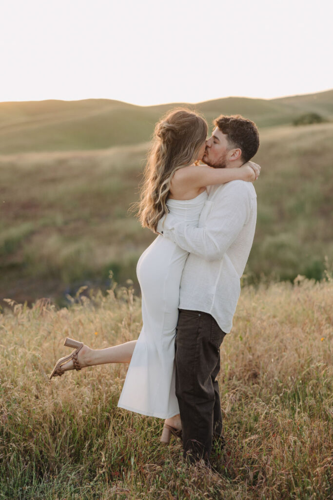 A man lifting up a woman and kissing her in a field. 