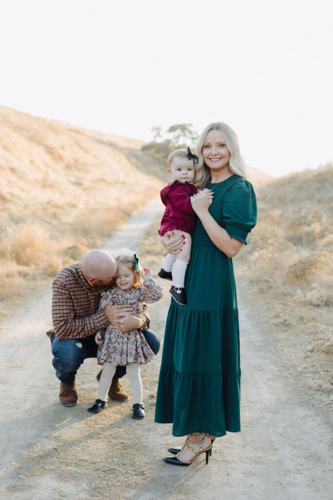 A family of four smiling and hugging on a dirt trail
