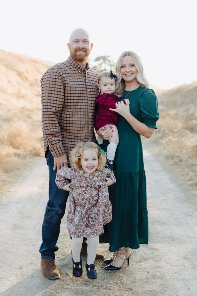 A family of four standing together with one child standing in front and the other behind held