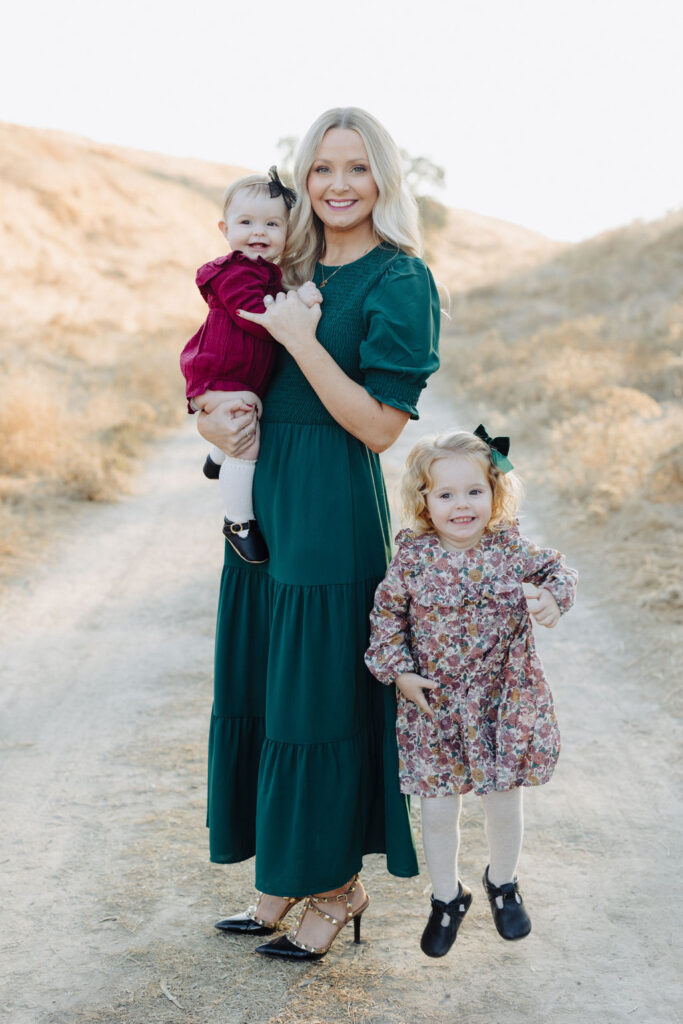 A mother holding a baby with a toddler jumping next to her