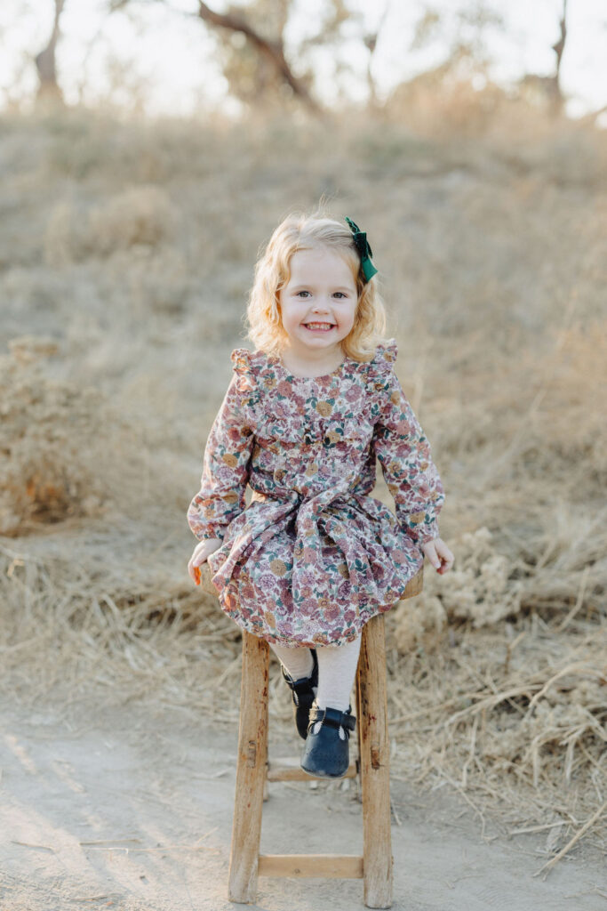 A toddler smiling and sitting on a stool 
